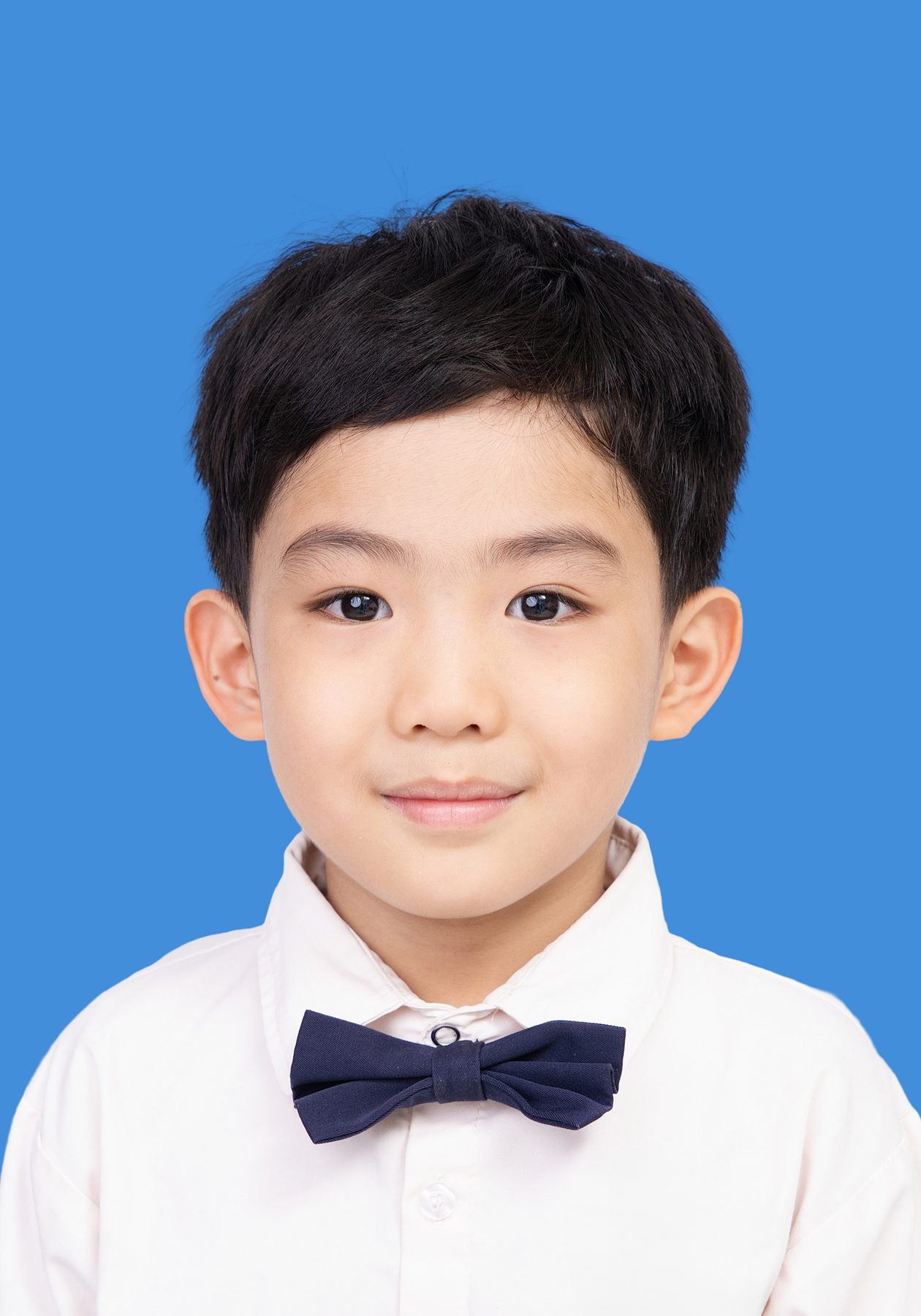 Premo Studio real client passport photo — young boy with bow tie, blue background